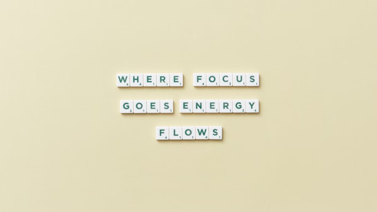 Inspirational quote 'Where Focus Goes Energy Flows' spelled with Scrabble tiles on a minimalist background.